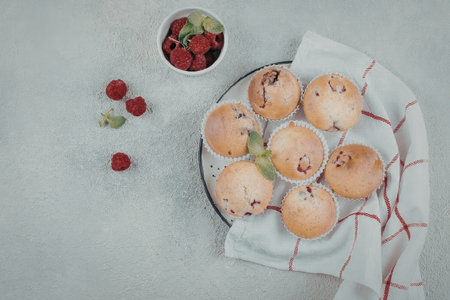 A plate of muffins with raspberries on the side, placed on a white and red towel.の写真素材