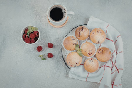Delicious muffins with raspberries and chocolate chips on a plate with a cup of coffee and fresh raspberriesの写真素材
