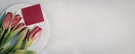 A bouquet of pink tulips on a white plate with a pink note on a white backgroundの写真素材