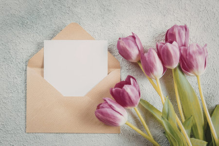 A bouquet of pink tulips placed beside an open brown envelope on a grey surface.の写真素材