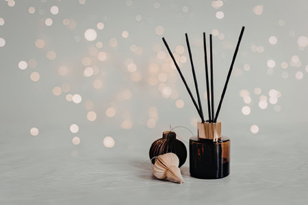 A reed diffuser with black sticks and a brown bottle sits next to two cones on a white surface with a bokeh background.の写真素材