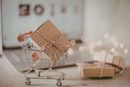 A small shopping cart with gift boxes and a laptop in the backgroundの写真素材