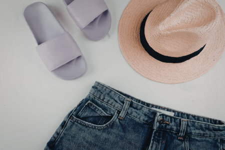A flat lay of summer clothing items including denim shorts, a straw hat, and purple sandals.の写真素材
