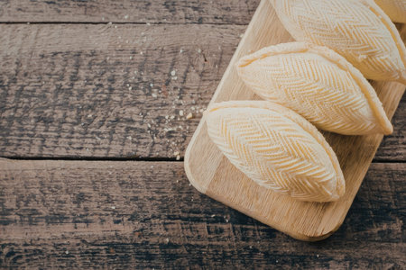 A wooden plate holding three empanadas on a rustic wooden tableの写真素材