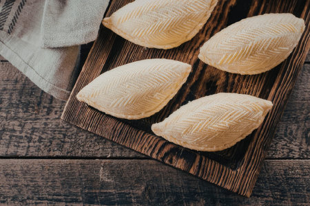 Four traditional Azerbaijani shekerbura pastries with detailed hand-carved patterns are arranged on a dark wooden board, placed on a rustic table with a linen cloth.の写真素材