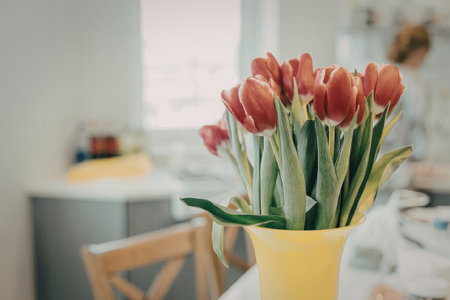 A bouquet of red tulips in a yellow vase on a kitchen table with a blurred background.の写真素材