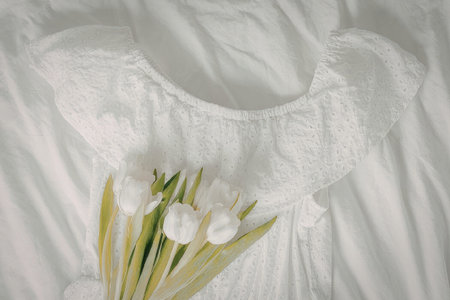 A white dress with a bouquet of tulips on a bed with white sheetsの写真素材