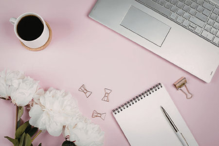 A laptop, coffee, flowers, and office supplies on a pink deskの写真素材