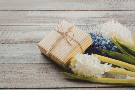 A beautifully wrapped gift with a bouquet of white and purple flowers on a rustic wooden tableの写真素材