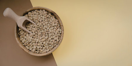 A wooden bowl filled with green beans and a scoop on a brown and yellow background