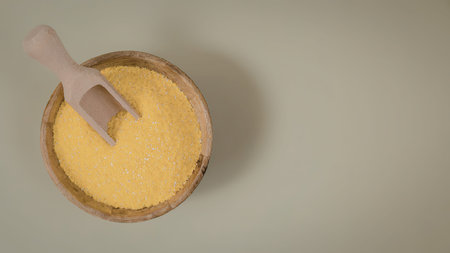 A wooden bowl filled with yellow granules and a small wooden scoop on top, set against a green...