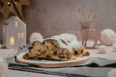 A slice of stollen cake with white icing on a plate, surrounded by festive decorations.