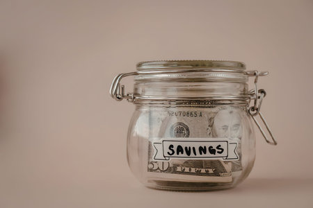 A clear glass jar with a metal clasp and a label that reads savings, sitting on a beige surface.