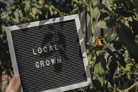 A hand holding a black sign with white text that reads 'LOOSE GROWING' in a garden with green leaves...