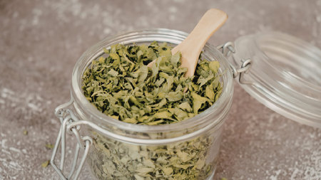 A glass jar filled with chopped green herbs and a wooden spoon, on a rustic surface.