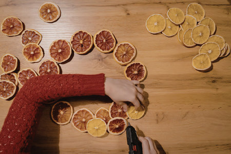 An individual wearing a red sweater is arranging dried orange and grapefruit slices into a circular pattern on a wooden surface.の写真素材
