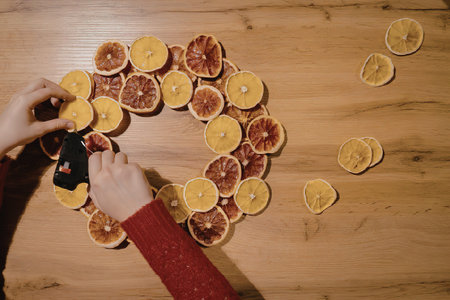 An overhead shot of a person arranging dried orange and blood orange slices into a decorative...
