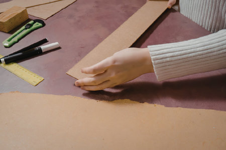 A person's arm and hand are visible as they work on a large sheet of brown paper, with a ruler and...
