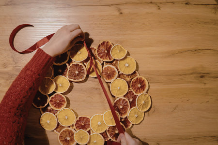 A person in a red sweater making a dried orange wreath on a wooden tableの写真素材