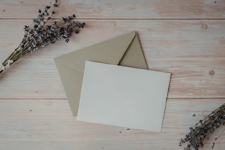 A green envelope and a blank white card on a wooden table with lavender flowersの写真素材