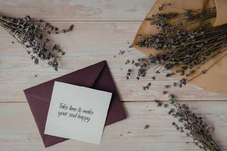 A white note on a purple envelope with dried lavender flowers scattered around on a wooden...