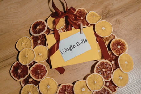 A circular wreath made of dried orange and blood orange slices, adorned with a red ribbon and a note...