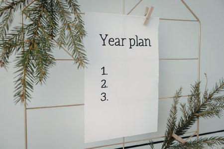 A white note with 'Year plan' and a numbered list on a clothespin with pine branches