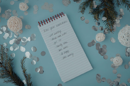 A spiral notebook with handwritten notes lies on a light blue surface surrounded by Christmas...