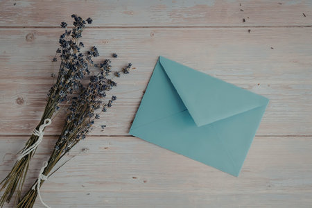 A light blue envelope on a wooden background with a bunch of lavender