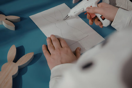 A child is engaged in a creative activity, using glue and paper to craft a design, with wooden...