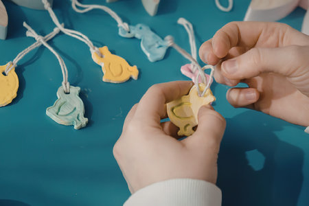 A child's hands holding a yellow Easter bunny decoration with other colorful decorations in the...