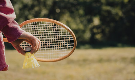 A child in a pink outfit holding a badminton racket with a shuttlecock in a grassy outdoor setting.