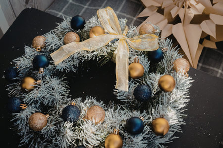 A Christmas wreath made of white tinsel with blue and gold ornaments and a gold ribbon tied in a bow at the top.の写真素材