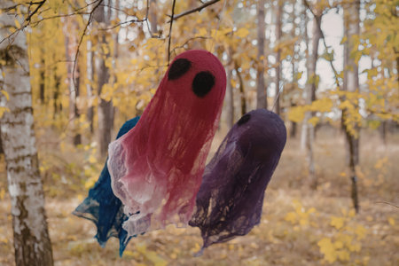 A blurry image of colorful ghost decorations hanging from a tree branch in a wooded area with yellow...