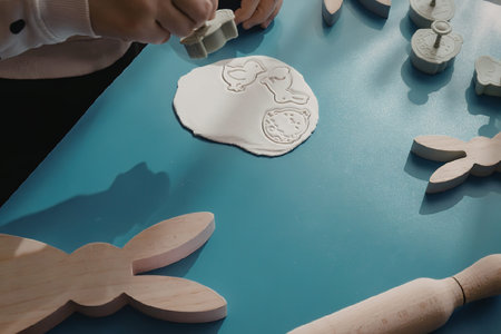 A person's hand holding a green object over a blue table with wooden Easter bunny shapes and a paper...
