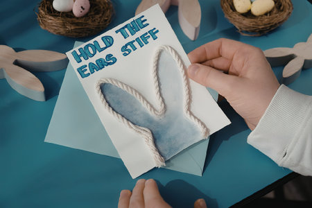 A child's hands holding a handmade Easter bunny card with a blue background and wooden Easter eggs
