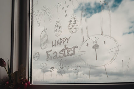 A child's drawing of an Easter bunny and eggs on a window with a cloudy sky in the background.
