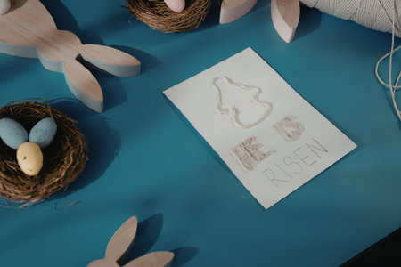 The image features a blue table with an Easter-themed arrangement. A white paper with a bunny...