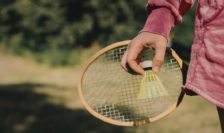 A girl in a pink jacket holding a badminton racket and shuttlecock outdoors