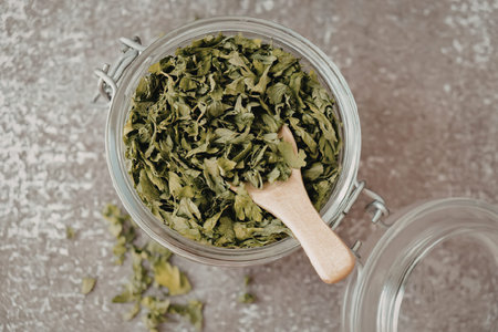 A glass jar filled with chopped green herbs and a wooden spoon, on a gray surface.