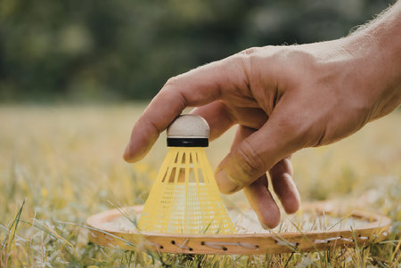 A hand holding a neon green badminton shuttlecock on a racket in a grassy field.の写真素材