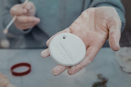 A person's hand holding a small, round, white ceramic disc with a hole at the top.