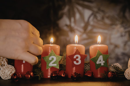 A hand lighting advent candles for Christmas, with four red candles and green stars with numbers on them.の写真素材