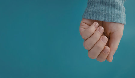 A close-up of a hand wearing a blue sweater cuff against a blue background