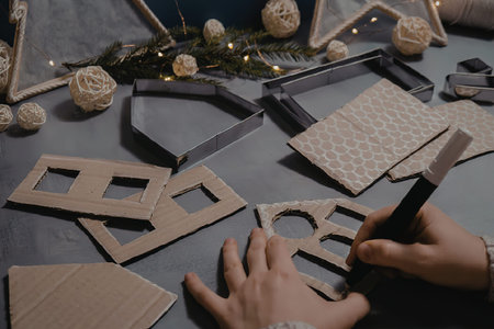 A person's hands are crafting wooden Christmas decorations on a table with various tools and materials.の写真素材