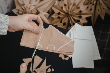 A hand tying a string around a brown paper envelope with white envelopes and paper snowflakes in the...
