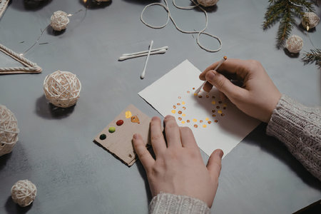A person is painting a holiday card on a table with various craft supplies.の写真素材