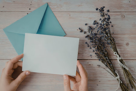 A person holding a blank white card with a light blue envelope and a bouquet of lavender flowers on...