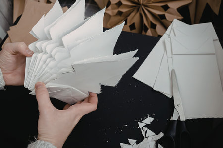 A person is folding white origami paper on a black table with other folded papers nearby.の写真素材