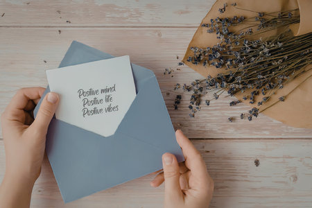 A pair of hands holding a light purple envelope with a white note on top and a brown plate with...